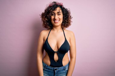 Yüzünde mutlu ve havalı bir gülümsemeyle pembe arka planda mayo ve güneş gözlüğü takan genç, güzel bir Arap kadın. Şanslı kişi..