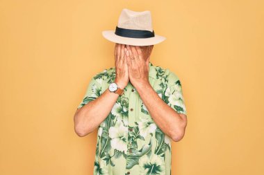 Plaj tatilinde yaz şapkası takan ve çiçekli gömlek giyen orta yaşlı, kır saçlı bir adam. Üzücü bir ifadeyle elleri ve ağlayarak yüzünü kapatıyor. Depresyon kavramı.