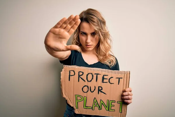 Young activist woman asking for environment holding banner with protect planet message with open hand doing stop sign with serious and confident expression, defense gesture
