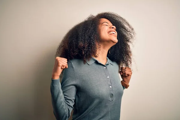Young beautiful african american woman with afro hair standing over isolated background very happy and excited doing winner gesture with arms raised, smiling and screaming for success. Celebration concept.
