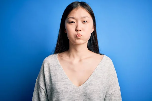 年轻美丽的亚洲女人穿着休闲装 站在蓝色孤立的背景上 脸上带着滑稽的表情 满嘴通气 满嘴疯狂的表情 — 图库照片