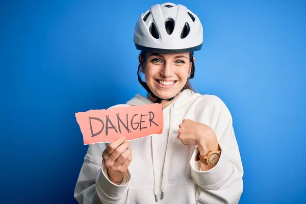 Young beautiful redhead cyclist woman wearing bike helmet holding danger paper message with surprise face pointing finger to himself
