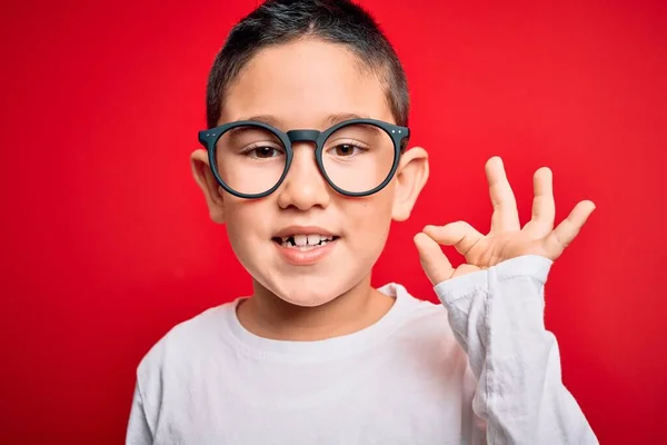 若いです小さなスマート男の子身に着けていますオタク眼鏡上の赤隔離された背景を行いますOk Signとともに指 優れたシンボル — ストック写真