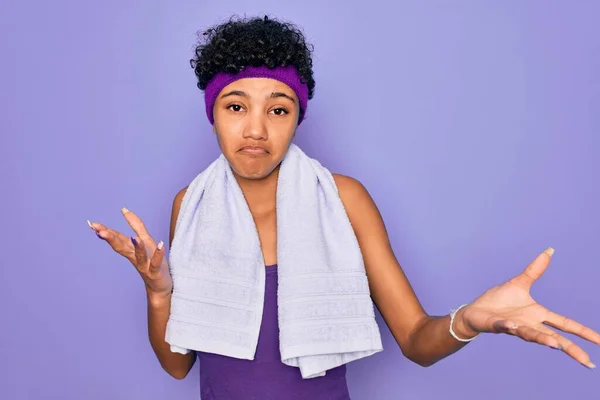 紫色の背景の上にタオルを着てスポーツをしている美しいアフリカ系アメリカ人のスポーティな女性は 腕や手で上げ混乱表現 疑いの概念 — ストック写真