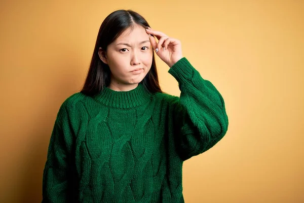 若いです美しいアジアの女性身に着けています緑の冬のセーター上の黄色隔離された背景心配し 額に手で問題について強調 神経と危機への不安 — ストック写真