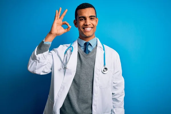 青い背景にコートと聴診器を身に着けているハンサムなアフリカ系アメリカ人医師は 手と指でOkサインをして積極的に笑顔 成功した表現 — ストック写真