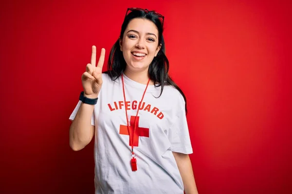 Young lifeguard woman wearing secury guard equipent over red background showing and pointing up with fingers number two while smiling confident and happy.