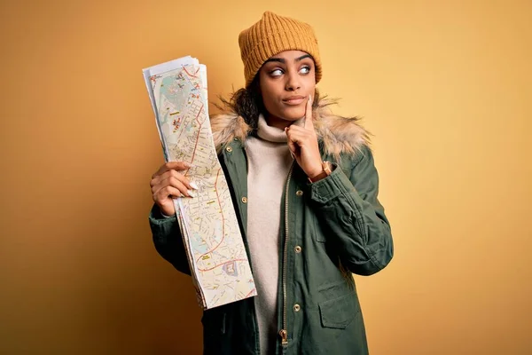 African american skier tourist girl wearing snow sportswear and ski goggles holding city map serious face thinking about question, very confused idea