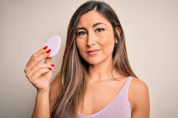 Молодая красивая женщина с помощью губки красоты с макияжем лица на розовом фоне с уверенным выражением на умное лицо, думая серьезно