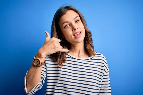 Young beautiful blonde girl wearing casual sweater standing over blue isolated background smiling doing phone gesture with hand and fingers like talking on the telephone. Communicating concepts.