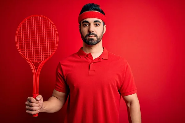 年轻英俊的运动员 留着胡子 用球拍在红色背景上打网球 聪明的脸上带着自信的表情 严肃地思考着 — 图库照片