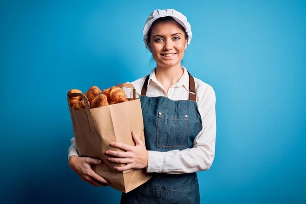 年轻美丽的面包师女人 蓝眼睛 头戴围裙 提着纸袋 脸上挂着幸福的表情 脸上挂着自信的微笑 露出牙齿 — 图库照片