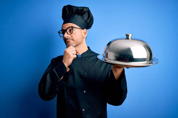 年轻英俊的厨师 身穿制服 头戴礼帽 拿着圆顶餐盘 严肃地思考着问题 非常迷惑的想法 — 图库照片