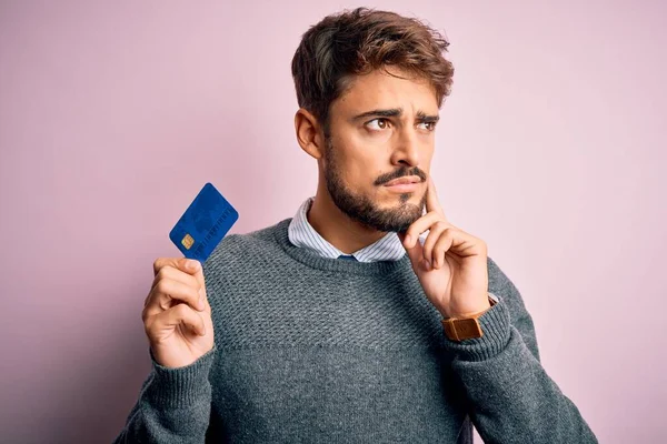 ピンクの背景深刻な顔の上に支払いのためのクレジットカードを保持ひげを持つ若い顧客の男質問について考えて 非常に混乱したアイデア — ストック写真