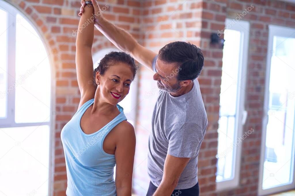 Middle age beautiful sporty couple smiling happy. Standing doing stretching after class ofyoga at gym