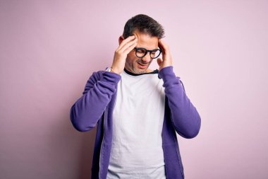 Mor eşofman altı giyen ve pembe arka planda duran gözlüklü genç ve yakışıklı bir adam. Baş ağrısı yüzünden. Migren ağrısı..
