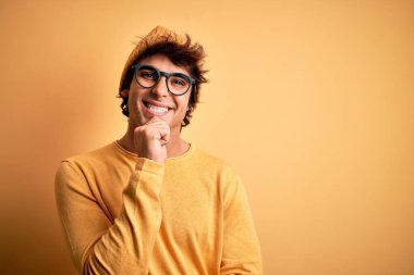 Üstü kapalı tişört ve gözlük takan genç yakışıklı bir adam izole edilmiş sarı arka planda kameraya bakıyor kollarını kavuşturup gülümseyerek ve çenesini kaldırarak bakıyor. Olumlu düşünüyorum..