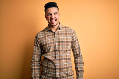 Genç yakışıklı adam rahat gömlek giyen izole sarı arka plan üzerinde duran komik ifade ile mutlu dil yapışmasını. Duygu kavramı.