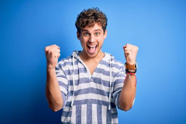 Kıvırcık saçlı, sıradan çizgili kazak giyen genç sarışın adam kolları açık ve açık bir şekilde başarıyı kutluyor ve şaşırıyor. Kazanan konsept.