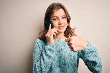 Sarışın genç bir kız akıllı telefondan konuşuyor, izole bir arka planda, mutlu bir şekilde gülümsüyor.