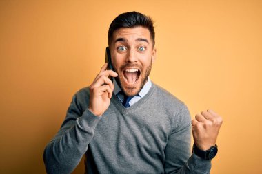 Genç yakışıklı adam sarı arka planda telefonla konuşuyor gururla bağırıyor ve zaferi ve başarıyı kutluyor çok heyecanlı, coşkulu bir duygu.