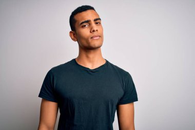 Genç, yakışıklı, Afro-Amerikan bir adam, günlük tişört giyiyor, beyaz arka plan üzerinde duruyor, uykulu ve yorgun görünüyor, yorgunluktan yorgun ve akşamdan kalma, sabahları tembel gözler..