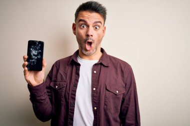 Kırık akıllı telefon tutan genç yakışıklı adam ekranda çatırdayan bir ekran gösteriyor. Şaşırmış bir yüzle korkmuş ve korku ifadesinden heyecanlanmış.