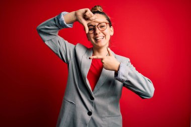 Mavi gözlü, gözlüklü, ceketli, gülümseyen, elleri ve parmakları mutlu yüzlü güzel sarışın iş kadını. Yaratıcılık ve fotoğrafçılık kavramı.