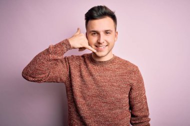 Pembe izole edilmiş arka planda günlük süveter giyen yakışıklı beyaz adam telefonla el ve parmaklarıyla telefonla konuşuyor gibi gülümsüyor. İletişim kavramları.