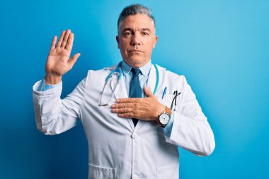 Orta yaşlı, yakışıklı, gri saçlı, ceketli ve mavi steteskoplu bir doktor. Elleri göğsünde ve avucunda açık yemin ediyor. Sadakat yemini ediyor.