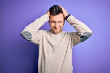 Mor izole edilmiş arka plan üzerine günlük süveter giyen yakışıklı beyaz bir adam acı ve migren yüzünden çaresiz ve stresli bir baş ağrısı çekiyor. Ellerini başının üstüne koy..
