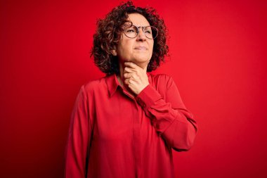 Orta yaşlı, kıvırcık saçlı, günlük gömlek giyen, kırmızı arka planda gözlük takan, boynu ağrıyan, boğaz ağrısı, grip ve enfeksiyon geçiren güzel bir kadın.