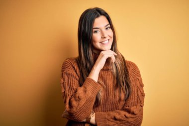 İzole edilmiş sarı arka plan üzerinde duran sıradan bir süveter giyen genç ve güzel bir kız kameraya kollarını kavuşturup gülümseyerek ve çenesini kaldırarak bakıyor. Olumlu düşünüyorum..