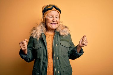 Kıdemli gri saçlı kayakçı kadın kar sporu kıyafetleri ve kayak gözlükleri takıyor. Kolları havada ve gözleri kapalı zaferi kutlarken gülümsüyor. Kazanan konsept.