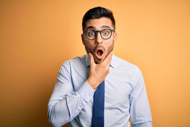 Sarı arka planda duran kravat ve gözlük takan genç yakışıklı işadamı elleri çenesinde olan inançsızlığa, şaşkınlığa ve hayrete düşmüş bir ifadeye bakıyor.