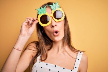 Sarı arka planda ananas güneş gözlüğü takan genç, güzel esmer kadın şaşırmış bir yüzle korkmuş ve korku ifadesinden heyecanlanmış.