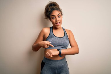 Genç Afro-Amerikan sporcu kadın spor giysisi giyiyor beyaz arka plan üzerinde Aceleyle saate, sabırsızlığa ve gecikmeye kızgın işaret ediyor