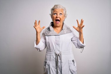 Son sınıf güzeli, gri saçlı, sıradan bir ceket giyen, beyaz arka planda duran çılgın ve sinirli bir kadın. Saldırgan bir ifadeyle bağırıyor ve kollarını kaldırıyor. Hayal kırıklığı konsepti.