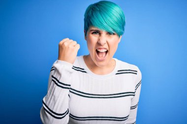 Mavi saçlı, sıradan bir süveter giyen genç ve güzel bir kadın stüdyo stüdyosunda sinirli ve kızgın duruyor öfkeyle bağırırken yumruğunu kaldırıyor. Öfke ve agresif kavram.