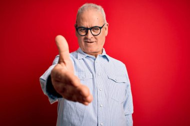 Orta yaşlı, yakışıklı, beyaz bir adam kırmızı arka planda günlük çizgili gömlek ve gözlük takıyor. Gülümsüyor, avuç içi kadar yardım ve kabul görüyor..