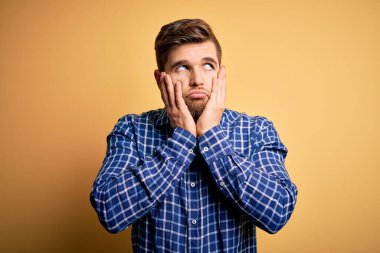 Sarışın, sakallı ve mavi gözlü genç bir işadamı sarı arka planda gömlek giyiyor. Yüzü, depresyonu ve üzüntüyü örten elleri yorulmuş, sorun yüzünden üzgün ve tedirgin.