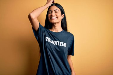 Sosyal yardım derneği ahlakı olarak gönüllü tişörtü giyen genç ve güzel bir İspanyol kadın. Gülümsüyor, el hareketleriyle saçlara dokunuyor, çekici ve şık poz veriyor.