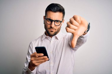Gözlük takan genç yakışıklı adam akıllı telefon ve kızgın yüzlü kulaklıklar kullanıyor. Negatif işaretler baş parmakları aşağıda, reddedilme konsepti ise reddediliyor.