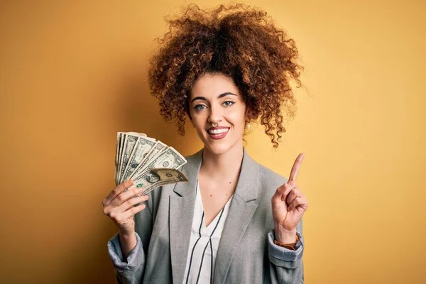 Kıvırcık saçlı ve elinde dolar olan güzel bir kadın bir fikir ya da soru işareti ile şaşırmış, mutlu yüzlü, bir numara.
