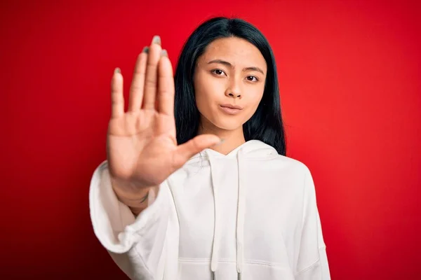 年轻美丽的中国女运动员穿着运动衫 披着孤立的红色背景 手心停止歌唱 脸上带有消极而严肃的手势的警告表情 — 图库照片