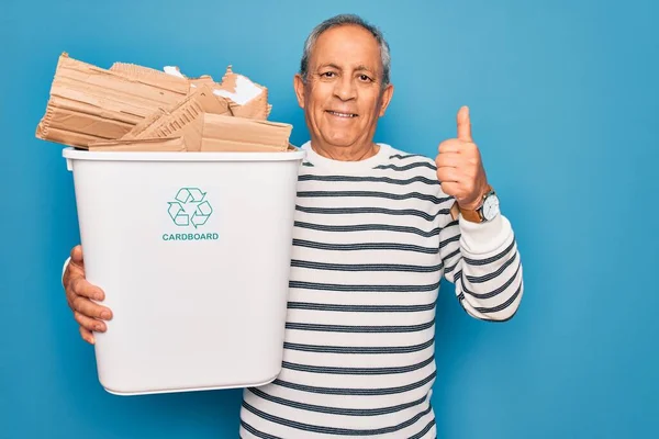 大きな笑顔で幸せな青色の背景をリサイクルするために段ボールでゴミ箱を保持シニア男はOkサインを行う 指で親指アップ 優れたサイン — ストック写真