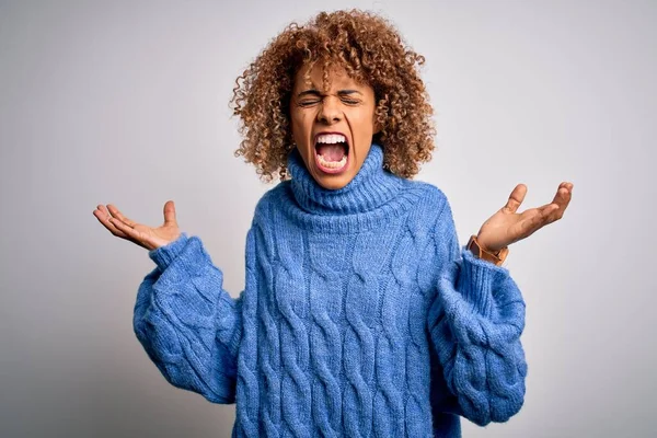 白い背景にタートルネックのセーターを着た若い美しいアフリカ系アメリカ人女性が狂気と怒りの叫びと積極的な表現と腕を上げて叫んでいます 欲求不満の概念 — ストック写真