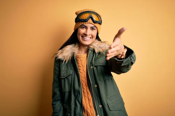冬の天候のためのスキーグラスとコートを身に着けている若い美しいヒスパニック系の女性は 挨拶や歓迎として握手を提供して笑顔 成功事業 — ストック写真