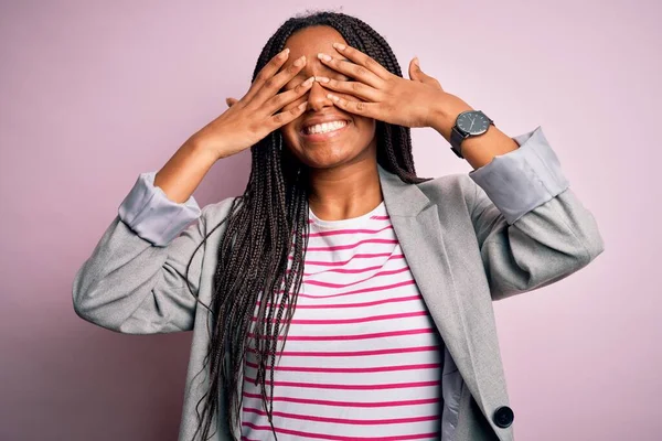 Genç Afro-Amerikalı iş kadını pembe izole edilmiş arka planda duruyor. Gözleri neşeli ve komik gülümseyen ellerle örtüyor. Kör kavram.