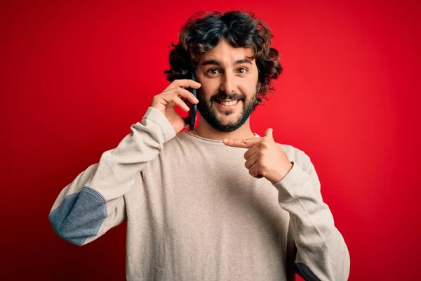 赤い背景の上にスマートフォンで話して会話を持っている髭を持つハンサムな男非常に幸せなポインティングで手と指 — ストック写真